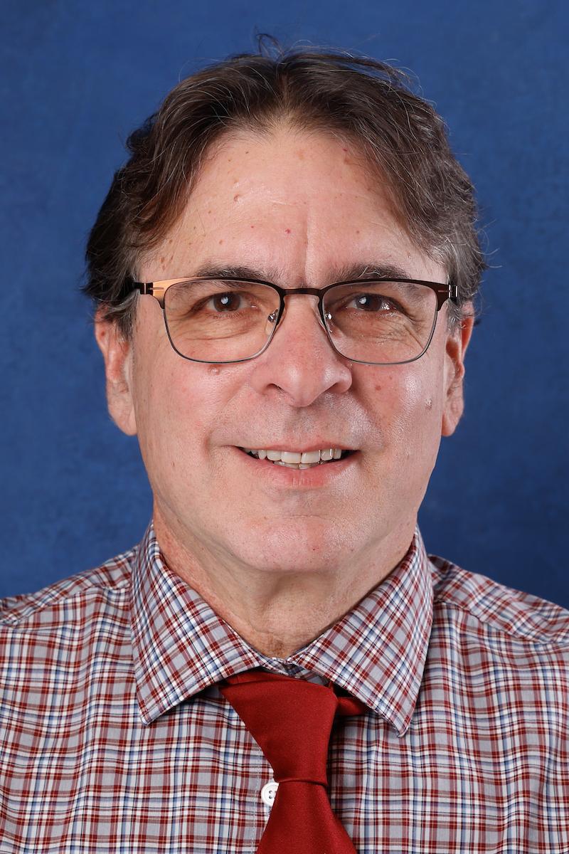 Dan Hanes, Ph.D., smiles in front of a blue background