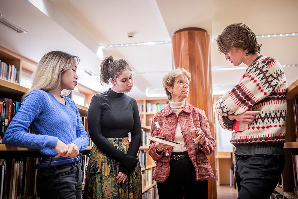 Encinar stands with students in discussion in a library.