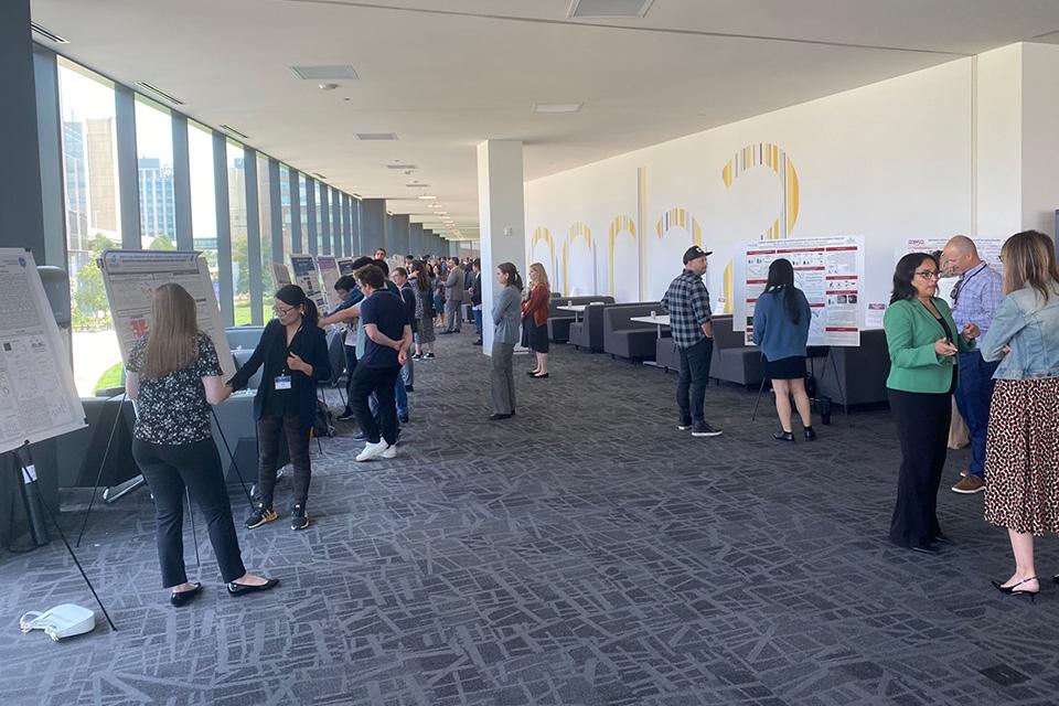 A corridor is lined with easels containing posters, while forum attendees look at the posters and have discussions.