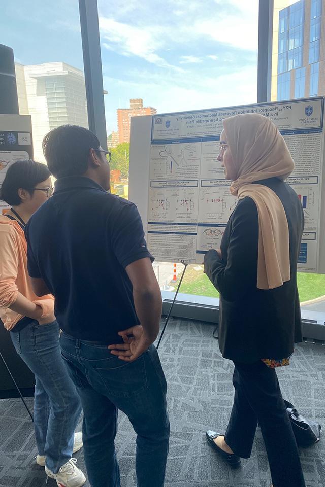 Two attendees hold a discussion in front of a research poster.