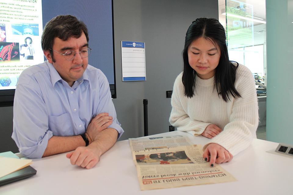 Klasen and Rogers sit at a table with a newspaper in front of them.